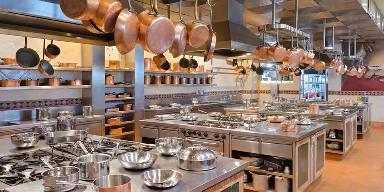Commercial kitchen with copper pans hanging over stainless steel prep stations