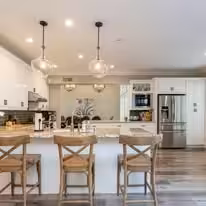 White kitchen with glass globe pendants over a long island and wooden cross back stools