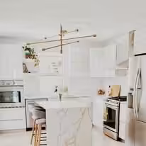 White kitchen with brass fittings, a marble island and a stainless range