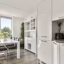 Handleless gloss white kitchen opening onto a dining table by a window