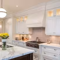 White kitchen with a custom hood, marble backsplash and a dark stained island