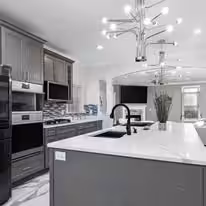 Gray island with white marble counters, a modern chandelier and stainless appliances