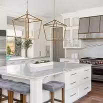 White kitchen with brass lantern pendants over a marble waterfall island
