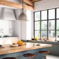 Teal island under an exposed beam with industrial pendants and black steel windows